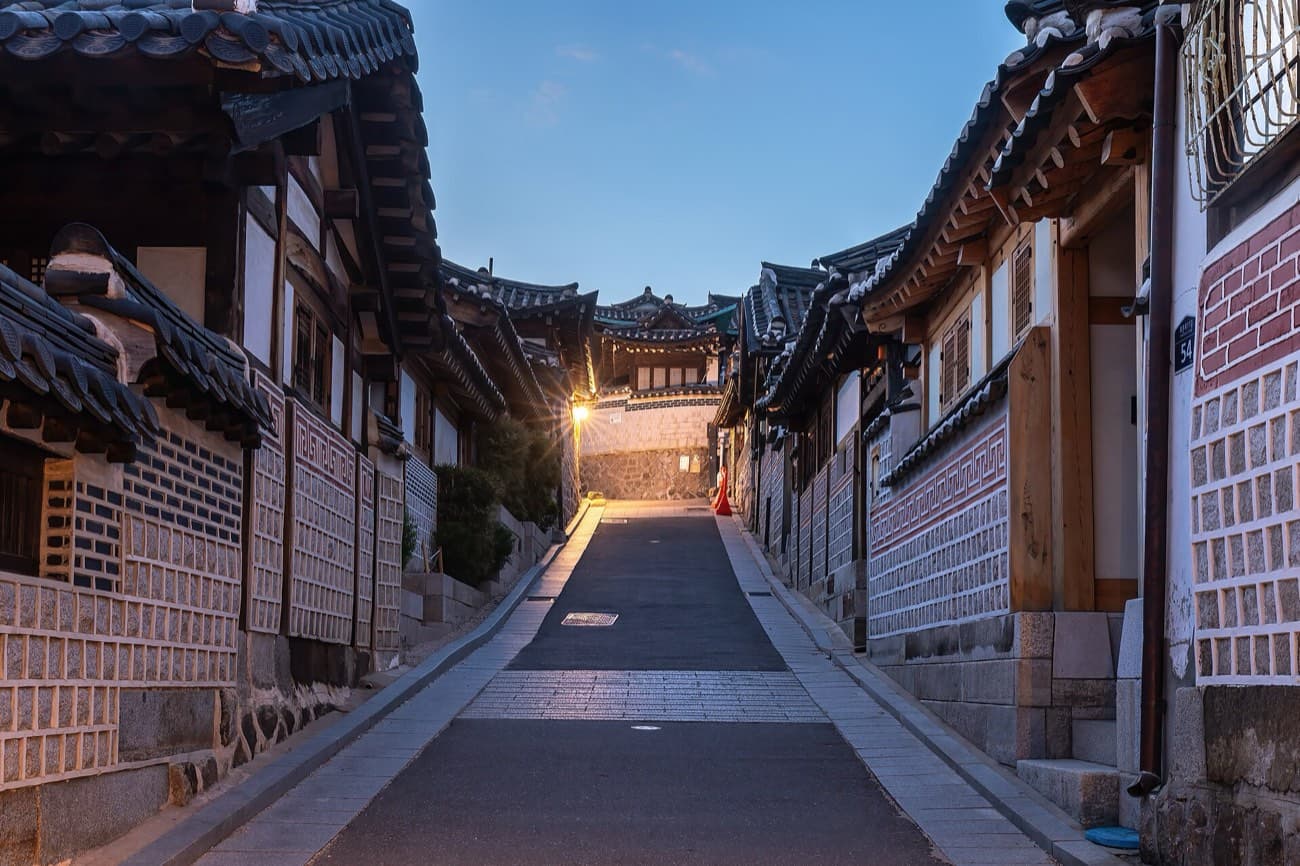 Una calle en subida de Bukchon, en Seúl, con casas hanok de techos de tejas y faroles encendidos a la hora azul